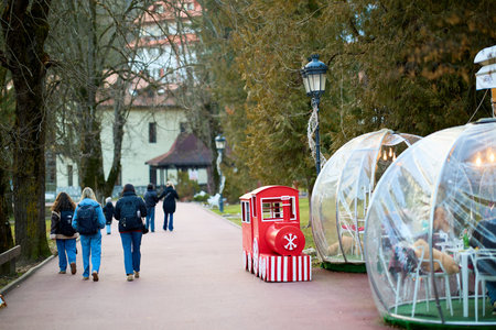 Park scene with red train, transparent domes, and people walking. December 13, 2025 Sinaia Romania.のeditorial素材