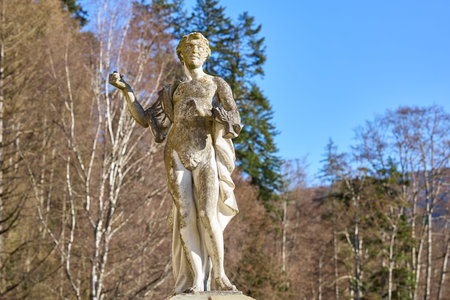 Ancient weathered stone statue in forest setting under clear blue sky. December 13, 2025 Sinaia Romania.のeditorial素材