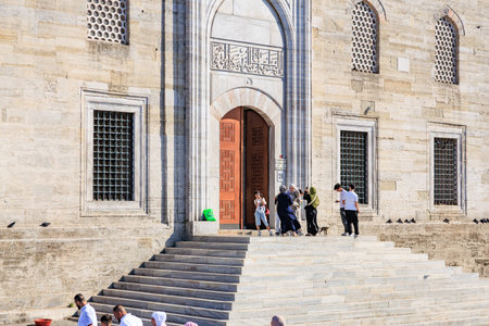 People visiting historic mosque entrance with stone architecture and arabic calligraphy. August 12,...