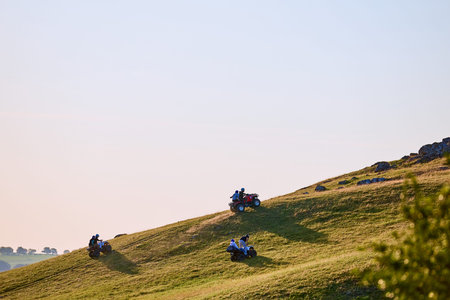 Three people riding atvs on sunny hillside.