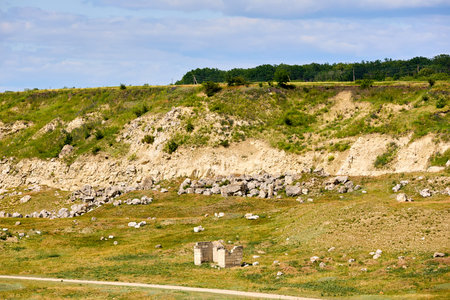 Rural landscape with rocky hillside and remote ruin under blue sky.の写真素材