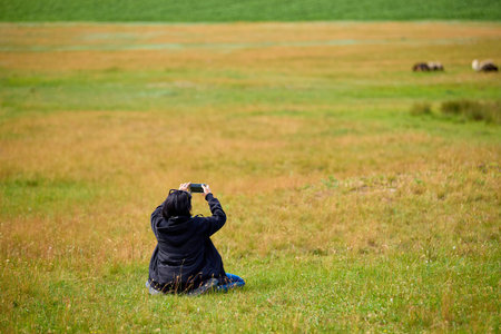 Asian female young adult taking photo in scenic field landscape.