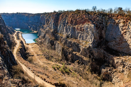 Stunning quarry landscape with serene lake and rugged cliffs under clear blue sky.