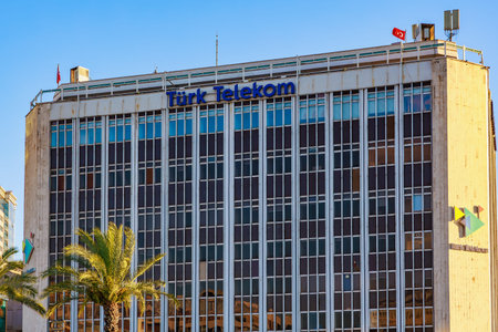 Turk telekom building exterior with palm trees and flag in urban setting during daytime. August 4, 2025 Izmir Turkey.のeditorial素材