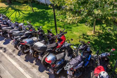 Row of parked motorcycles on sunny street with green grass and trees. August 12, 2025 Istanbul...