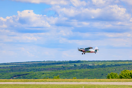 Vintage biplane landing on grass field under partly cloudy sky in countryside setting. May 31, 2025...