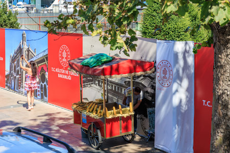 Street corn vendor in urban setting with red cart and cultural banners. August 12, 2025 Istanbul...