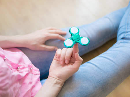 Girl playing with a glossy light colourful hand fidget spinner toyの写真素材