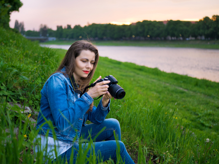 Beautiful girl tourist in a cotton jacket taking photos with a professional camera on the banks of...