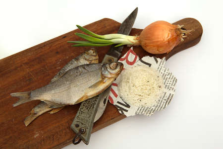 Dried fish, onions, old knife and salt on a board on a white background