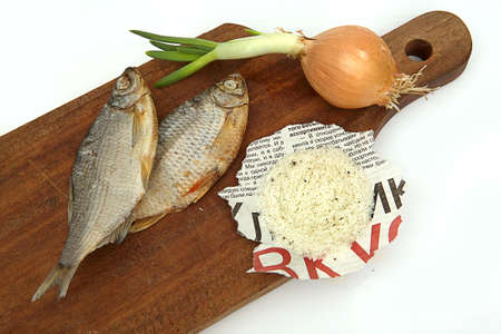 Dried fish, onions and salt on a board on a white backgroundの写真素材