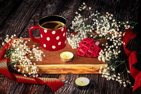 Red cup with white polka dots, candles, red knitted heart, gypsophila flowers and red ribbon. Romantic composition on a dark wooden background. Concept for Valentine's Dayの写真素材