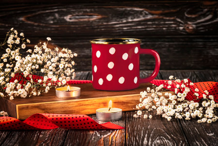 Red cup with white polka dots, candles, gypsophila flowers and red ribbon. Romantic composition on a dark wooden background. Concept for Valentine's Dayの写真素材