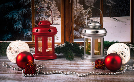 Red and silver lanterns with candles on the background of the window. Christmas balls, necklace, toys and fir branches as decor. Merry christmas concept.の写真素材