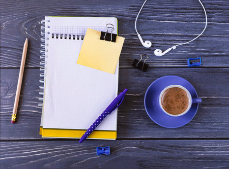 business background. Top view of workplace with notebooks, pen, pencil, headphones and blue cup of coffee on dark table.の写真素材