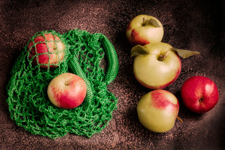 Ripe red apples in green string bag on dark background. fresh harvest of applesの写真素材