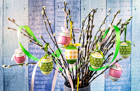 Easter eggs and willow branches in vase on wooden backgroundの写真素材