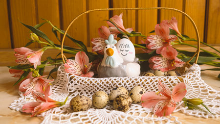 Easter basket with quail eggs and flowers. Decorative chicken with egg with a smile. Pink alstroemerias around.の写真素材