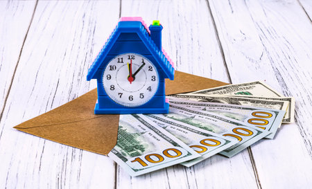 real estate loan concept. Dollar bills in an envelope and an alarm clock in the form of a house. Investments in real estate construction.の写真素材