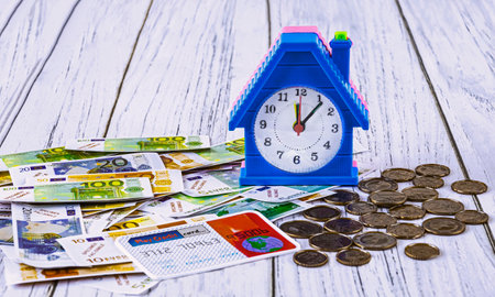 home loan concept. Toy euro banknotes and cents, credit card, alarm clock in the form of a house on a blue background.の写真素材