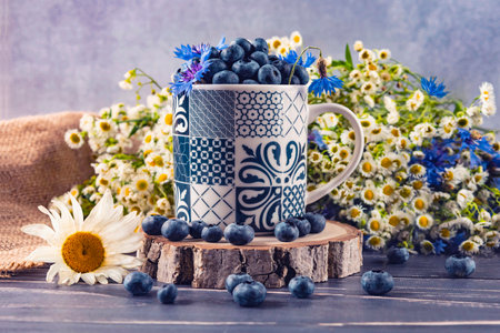 Blueberry and chamomile bouquet in a cup on a wooden backgroundの写真素材