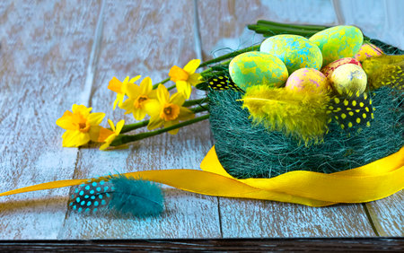Nest with easter eggs and feathers, yellow daffodil flowers and yellow ribbon, close up view. Happy Easter concept.の写真素材
