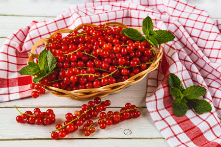 Red currant in a wicker basket on a white wooden backgroundの写真素材