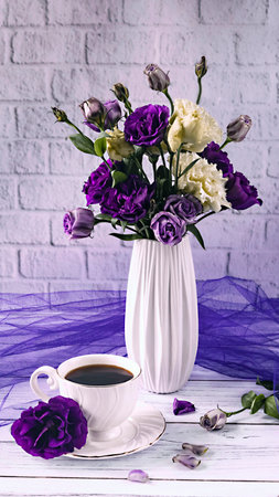 Purple and white eustoma flowers in a white vase on a white background. White cup of coffee on the table. Romantic still lifeの写真素材