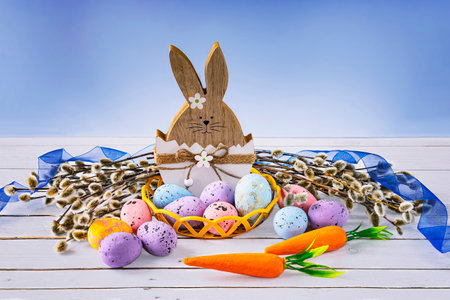Easter bunny with easter eggs, carrot and willow and blue ribbon. Festive Easter composition on a blue background.の写真素材