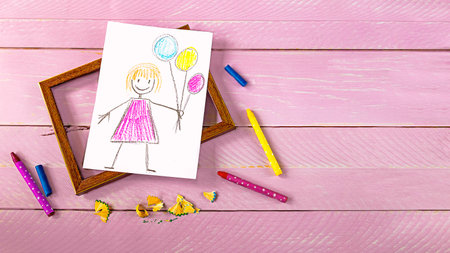 Colorful pencils and picture frame with drawing of happy girl on wooden background. mother's day conceptの写真素材