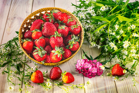 A harvest of ripe strawberries in a basket and a bouquet of wild flowers. Summer still lifeの写真素材