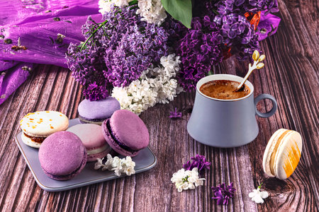 Cup of coffee with macaroons and lilac flowers on wooden backgroundの写真素材