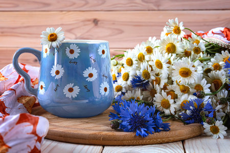 A blue cup of coffee with daisies and a beautiful bouquet of daisies and cornflowers. Summer still life with wildflowersの写真素材