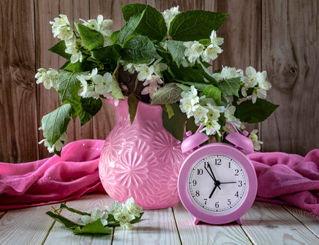 Alarm clock and bouquet of jasmine flowers on wooden backgroundの写真素材