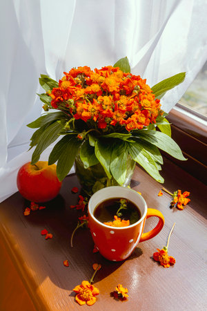 Bouquet of orange spring flowers on the window in the sunlight. Orange cup and red apple. spring...