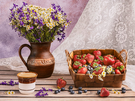 Basket with strawberries, blueberries, daisies and a cup of coffee on a wooden tableの写真素材