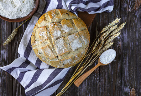 Composition with freshly baked rye bread with flax seeds, ears of wheat, flour on a rustic wooden...