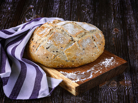 Freshly baked rye bread with flax seeds, linen towel, wooden tray on dark rustic background.の写真素材