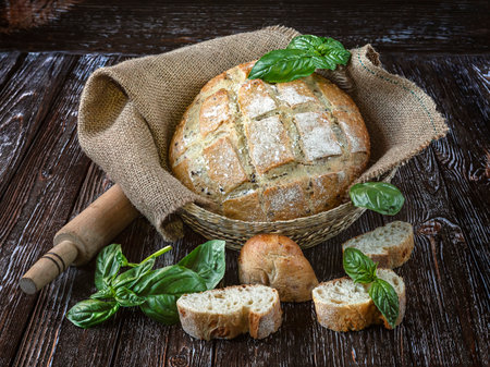 Freshly baked bread with basil in a basket on a wooden tableの写真素材