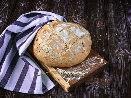 Freshly baked bread with flax seeds, linen towel, wooden tray on dark rustic background. View from aboveの写真素材