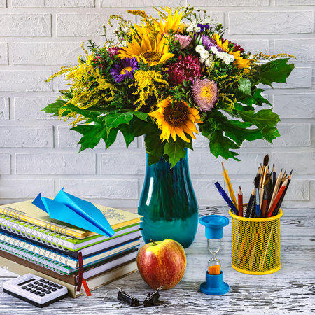 Back to school concept. Stationery, notebooks, paper airplane, apple, hourglass and vase with autumn flowers on white backgroundの写真素材