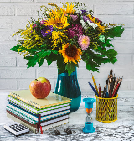 Back to school concept. Stationery, notebooks, apple, hourglass and vase with autumn flowers on white backgroundの写真素材