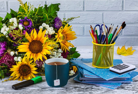back to school. A stack of school notebooks, stationery, a bouquet of autumn flowers, a blue cup of tea on a white background.の写真素材