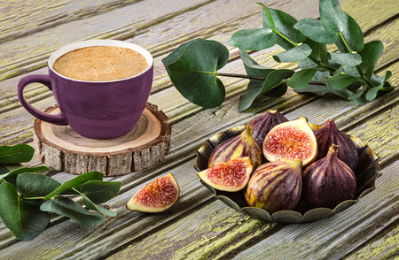 Fresh ripe figs on vintage plate, purple cup of coffee, sprig of eucalyptus, vintage scissors as decor on wooden background.の写真素材