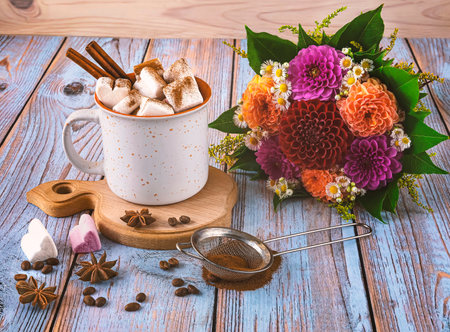 Cup of coffee with marshmallows, cinnamon sticks and and a bouquet of chrysanthemum flowers. Autumn still life on wooden backgroundの写真素材