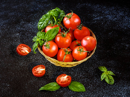 Ripe red tomatoes with basil in a basket on a black backgroundの写真素材