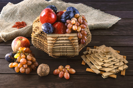 Harvest of ripe apples, plums, grapes in vintage basket, sunflower flower on wooden background and burlap. Autumn still lifeの写真素材
