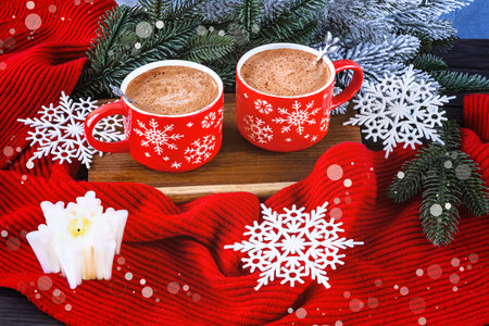 Christmas composition with two red coffee cups, snowflakes, lollipop, burning white candle, Christmas tree branches, red scarf on snowy background.の写真素材