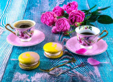 Cup of coffee with macaroons and roses on wooden backgroundの写真素材