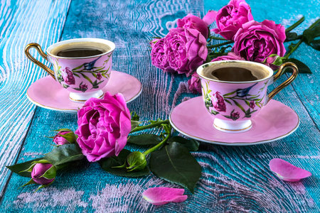 Two cups of coffee with pink roses on a blue wooden background.の写真素材